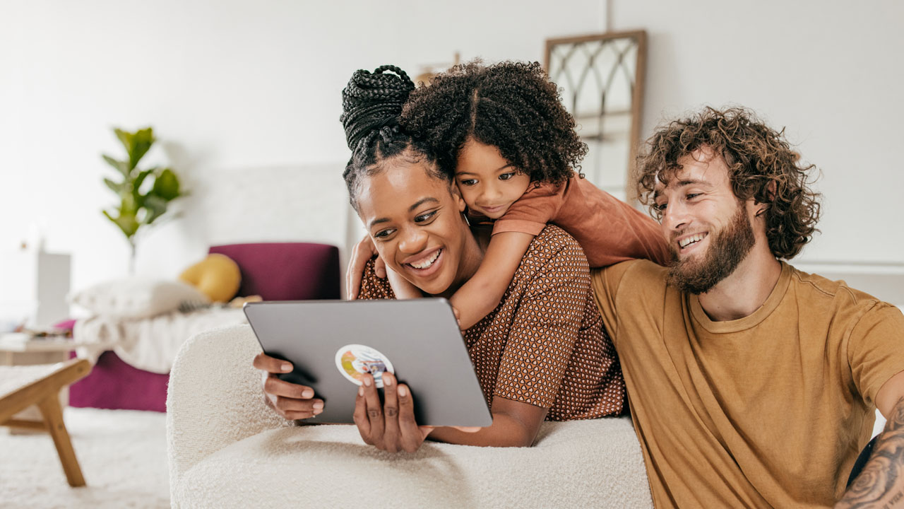 Their daughter hugging the mother behind while they checking the tablet device